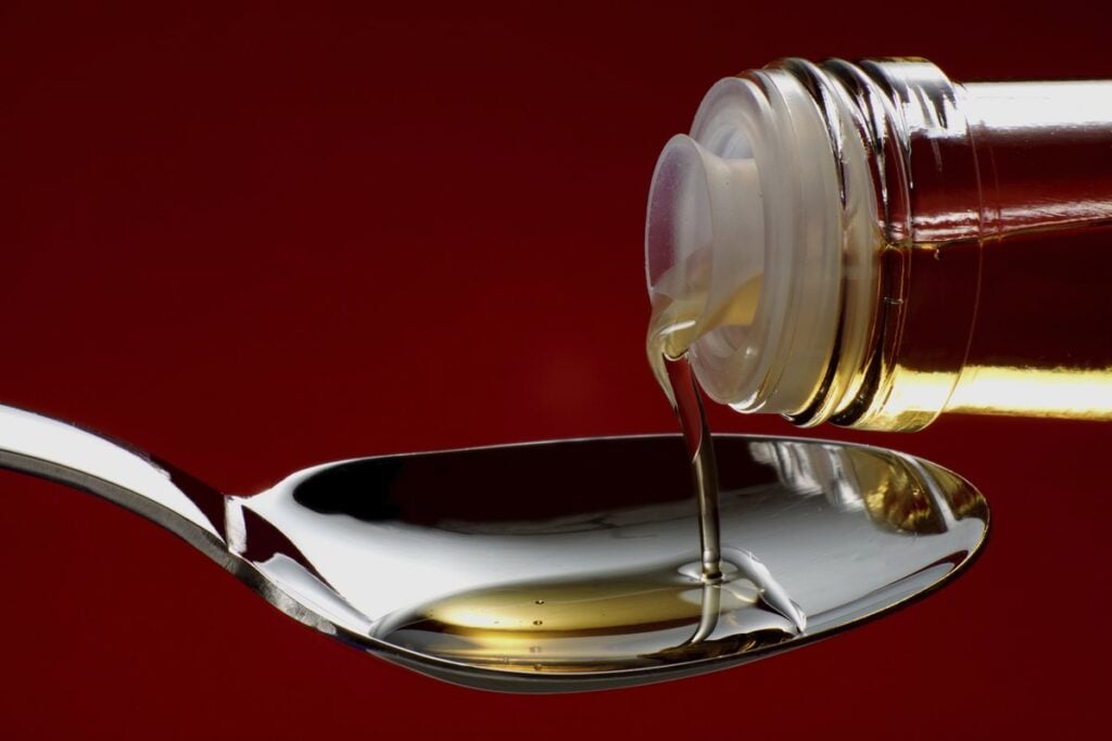 Huile versée d’un flacon dans une cuillère en métal, comme on mesure l’huile de foie de morue liquide