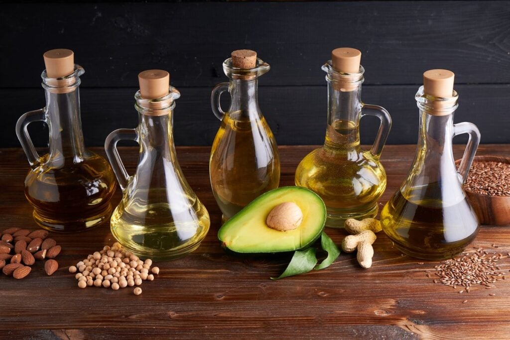Huiles végétales en carafes de verre à côté d’un avocat, d’amandes, de pois chiches et de graines de lin